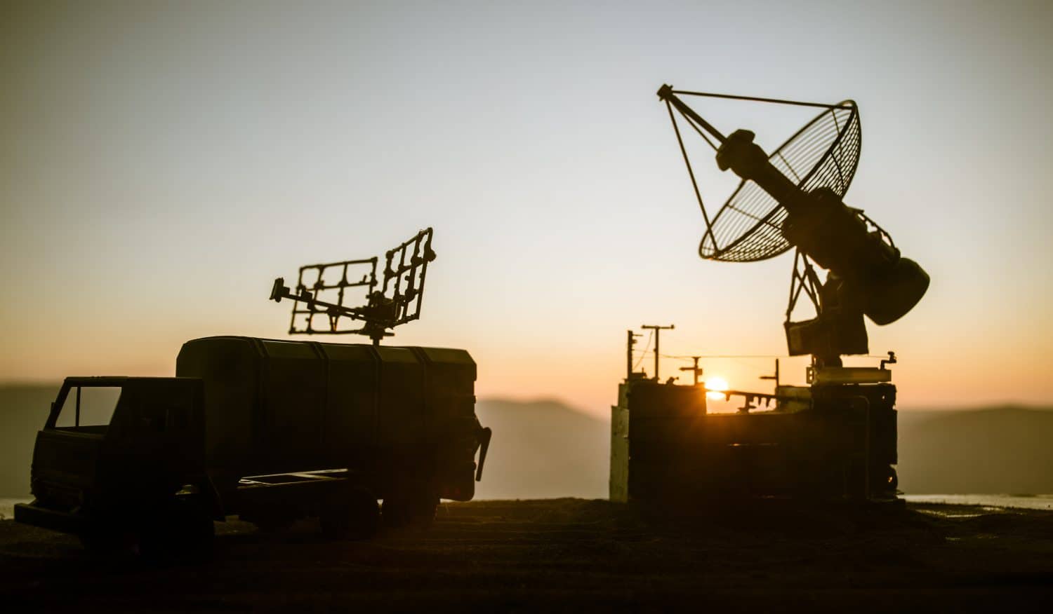 Creative artwork decoration. Silhouette of mobile air defence truck with radar antenna during sunset. Satellite dishes or radio antennas against evening sky. Selective focus