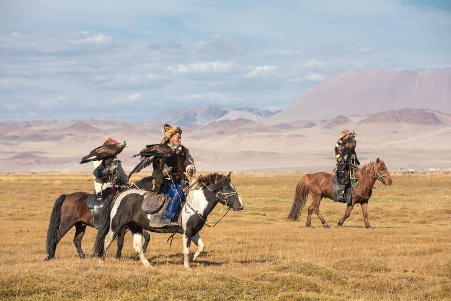 A group of traditional kazakh eagle hunters posing with their eagles and horses. Ulgii, Mongolia.