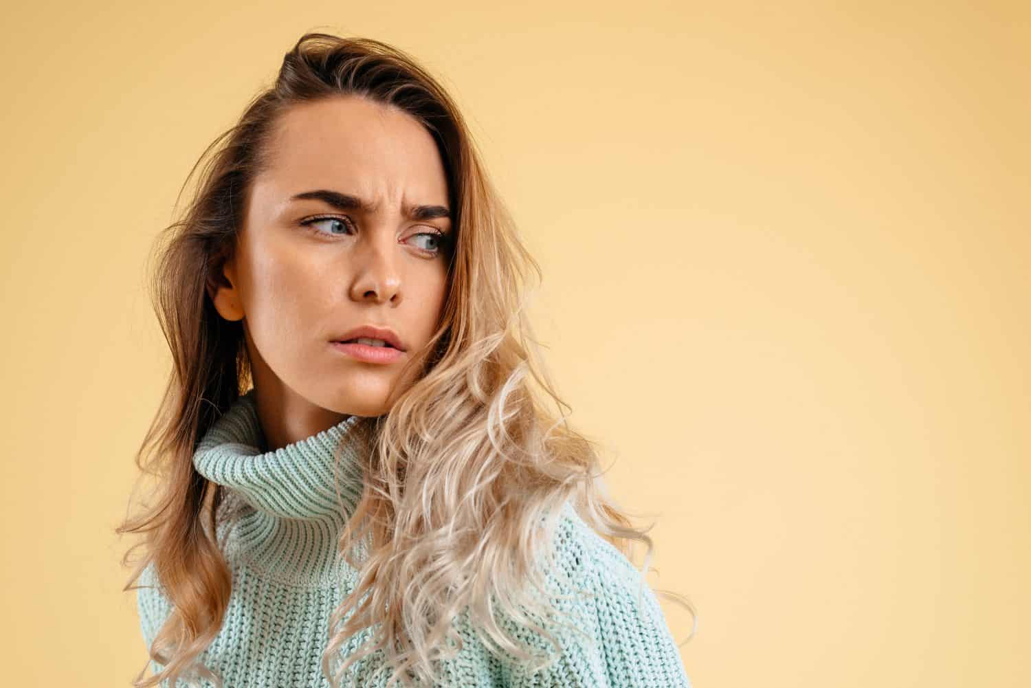 Suspicion. Doubt, mistrust concept. Doubtful woman looking with disbelief expression. Young beautiful emotional woman. Human emotions, facial expression concept. Studio. Isolated on yellow background