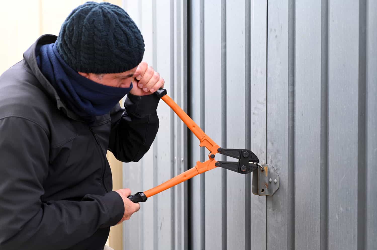 Burglar using bolt cutters to cut a door locker into home garage door. Crime insurance concept. Real people. Copy space