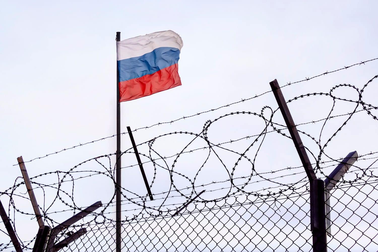 View of russian flag behind barbed wire against cloudy sky. Concept anti-Russian sanctions. A border post on the border of Russia. cancel culture Russia in the world