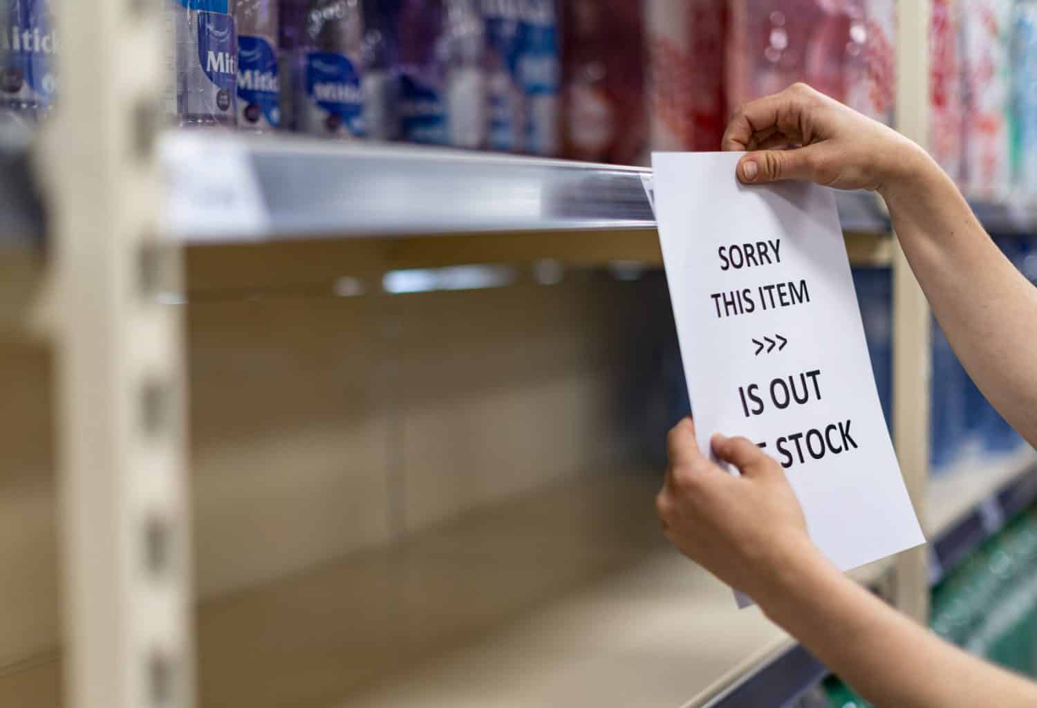 Shop assistant hanging a notice in empty shelves in a grocery store