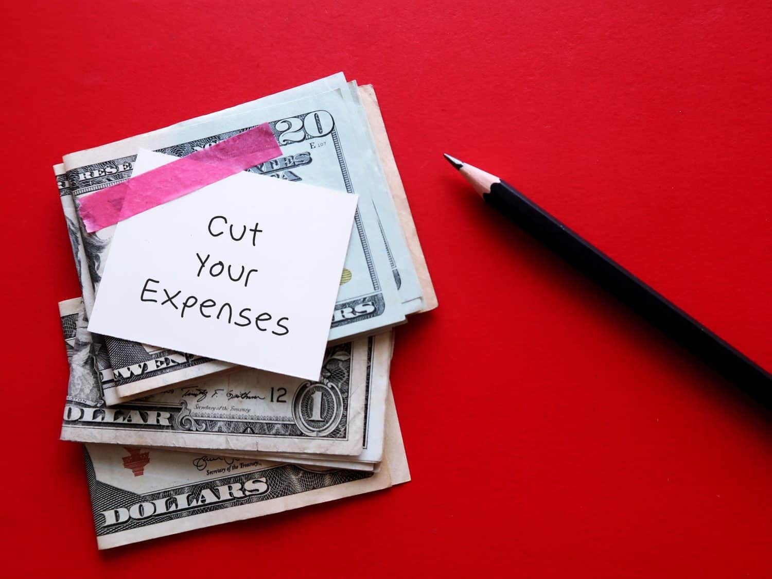 Cash dollars money on red background with handwritten text note CUT YOUR EXPENSES, means to cut or reduce household or business expenses to regaining control of your financial budget