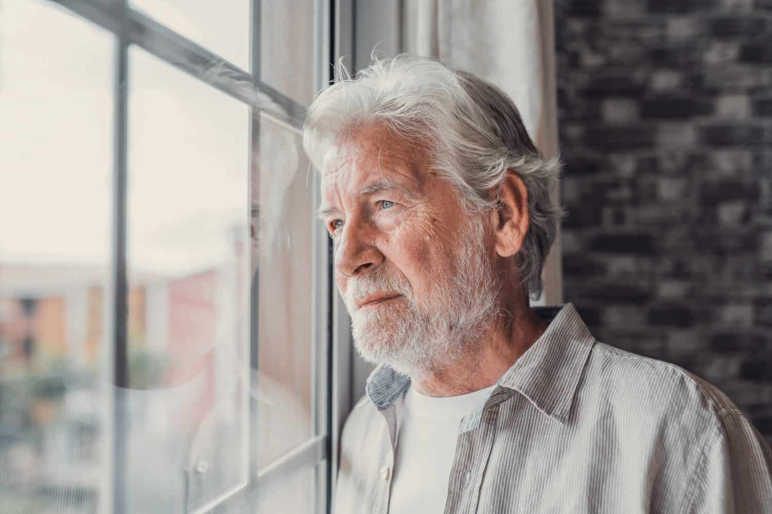 Pensive elderly mature senior man in eyeglasses looking in distance out of window, thinking of personal problems. Lost in thoughts elderly middle aged grandfather suffering from loneliness, copy space