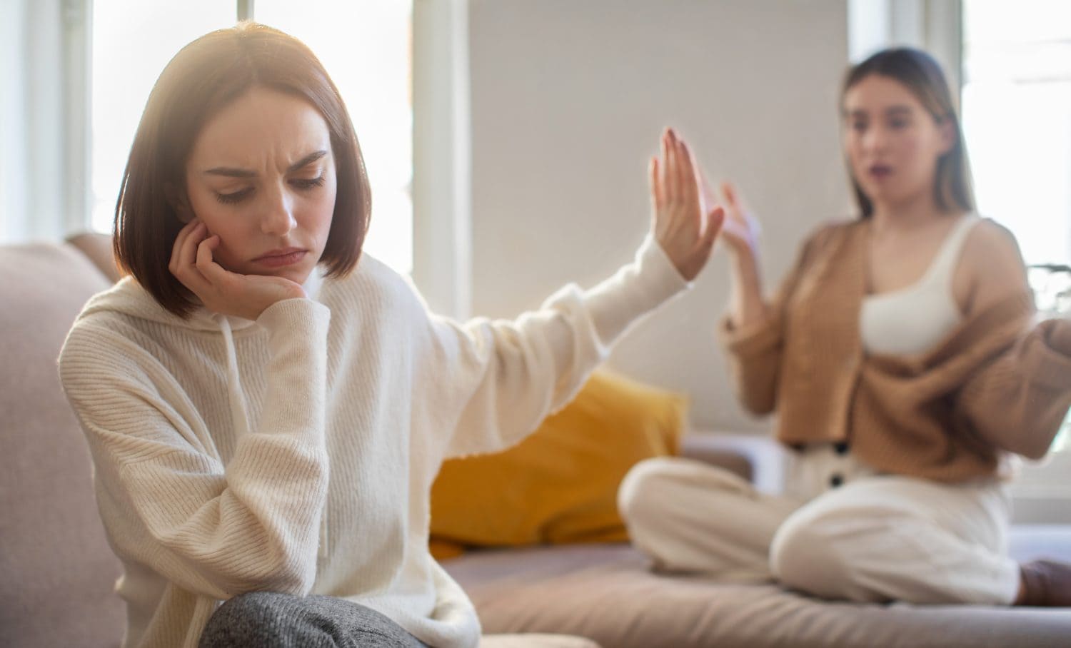 Offended sad european millennial lady ignores screaming displeased girlfriend, making stop sign with hand in living room interior. Scandal, quarrel and relationship problems at home, people emotions