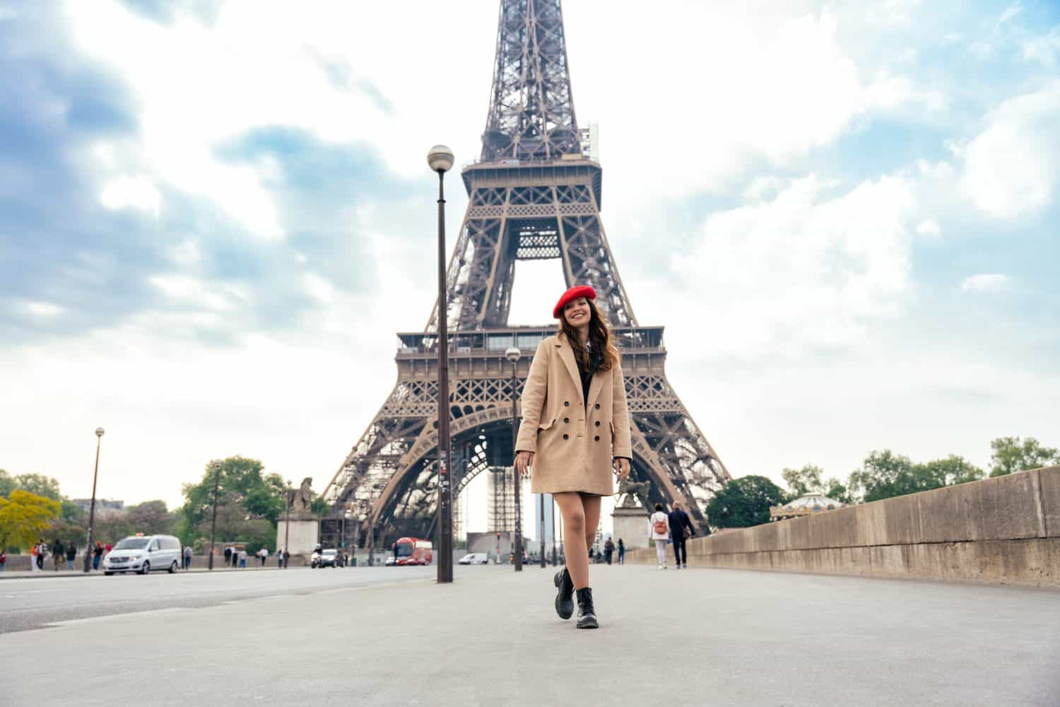 Beautiful young woman visiting paris and the eiffel tower. Parisian girl with red hat and fashionable clothes having fun in the city center and landmarks area