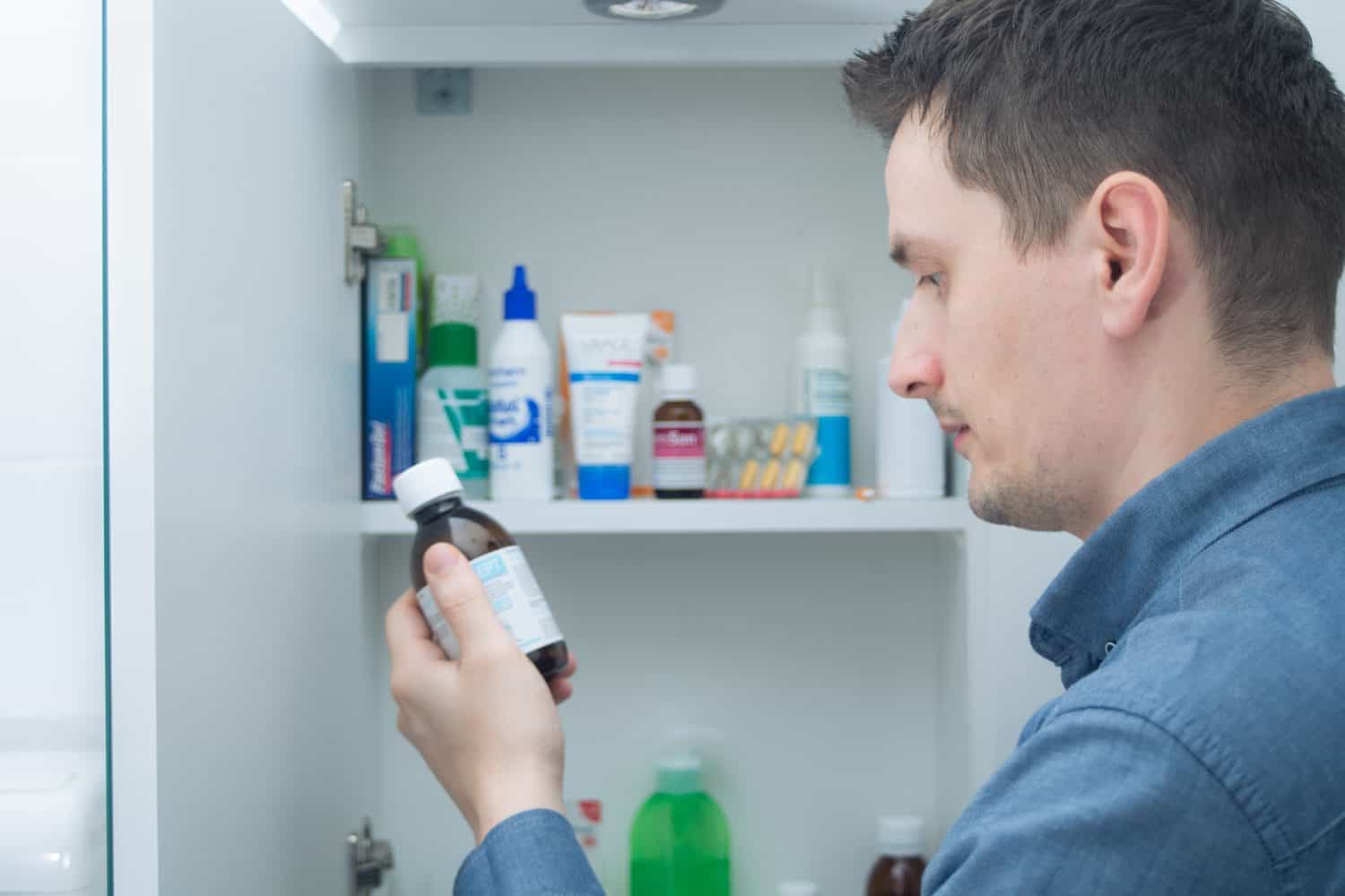 Man hold medication bottle reading instruction or prescription on packaging. Man looking at bottles from medicine cabinet