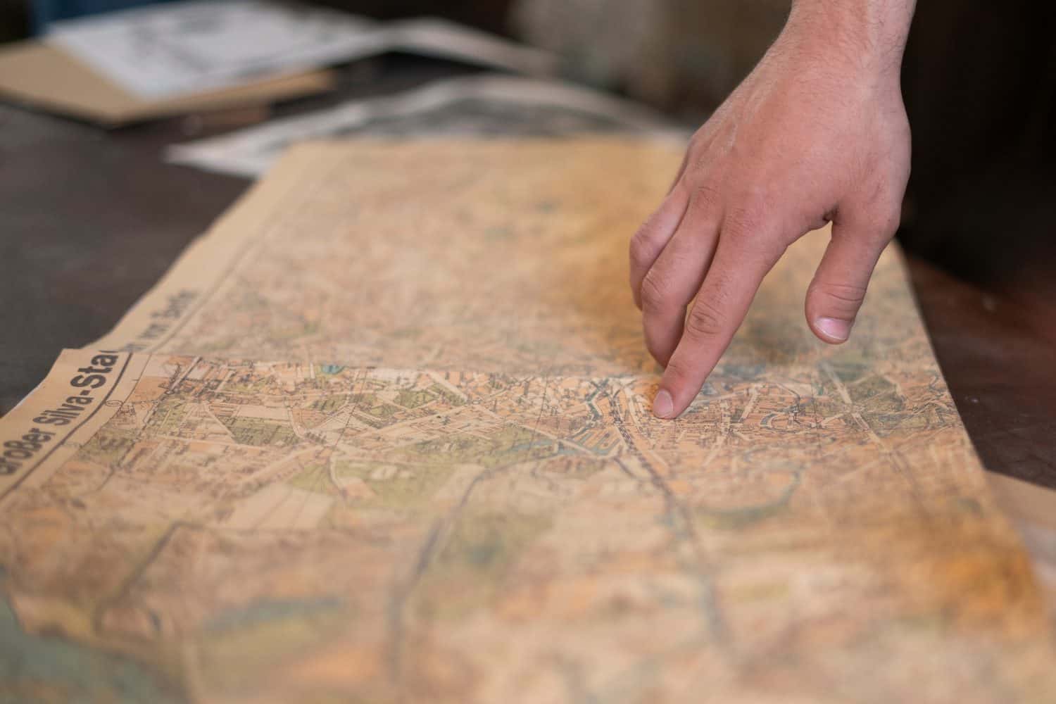 a person&#039;s finger pointing on the old map to go to the destination