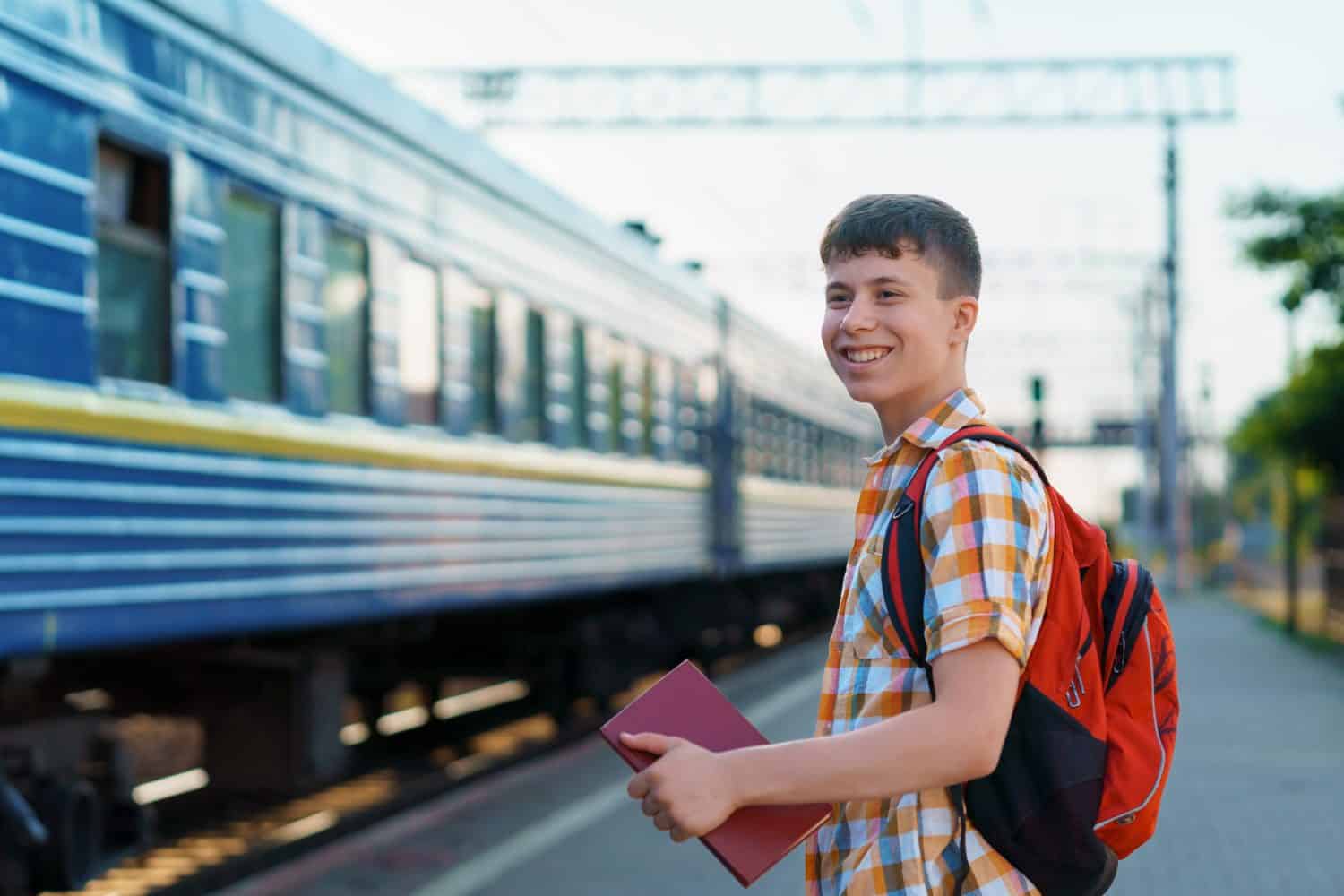 a student poses at a railway station, a teenage boy walks along the platform to the train, he has a backpack and books, goes to study, the concept of education