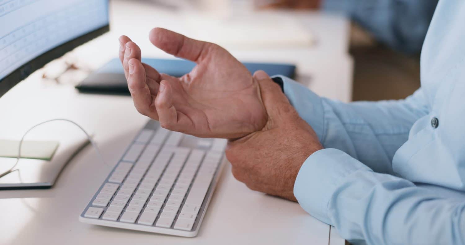 Businessman, hands and wrist in joint pain from injury, overworked or carpal tunnel syndrome at office. Closeup of man or employee with arthritis, ache or inflammation of palm on desk at workplace