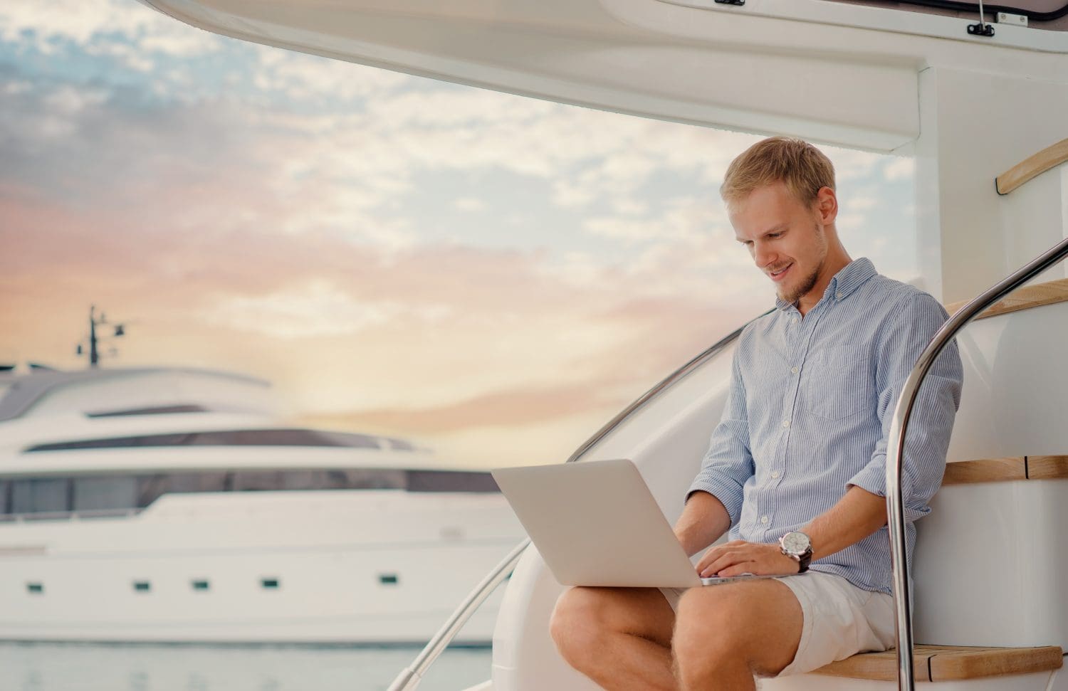 Luxury traveling and working. Handsome young man using laptop on the deck of modern yacht.