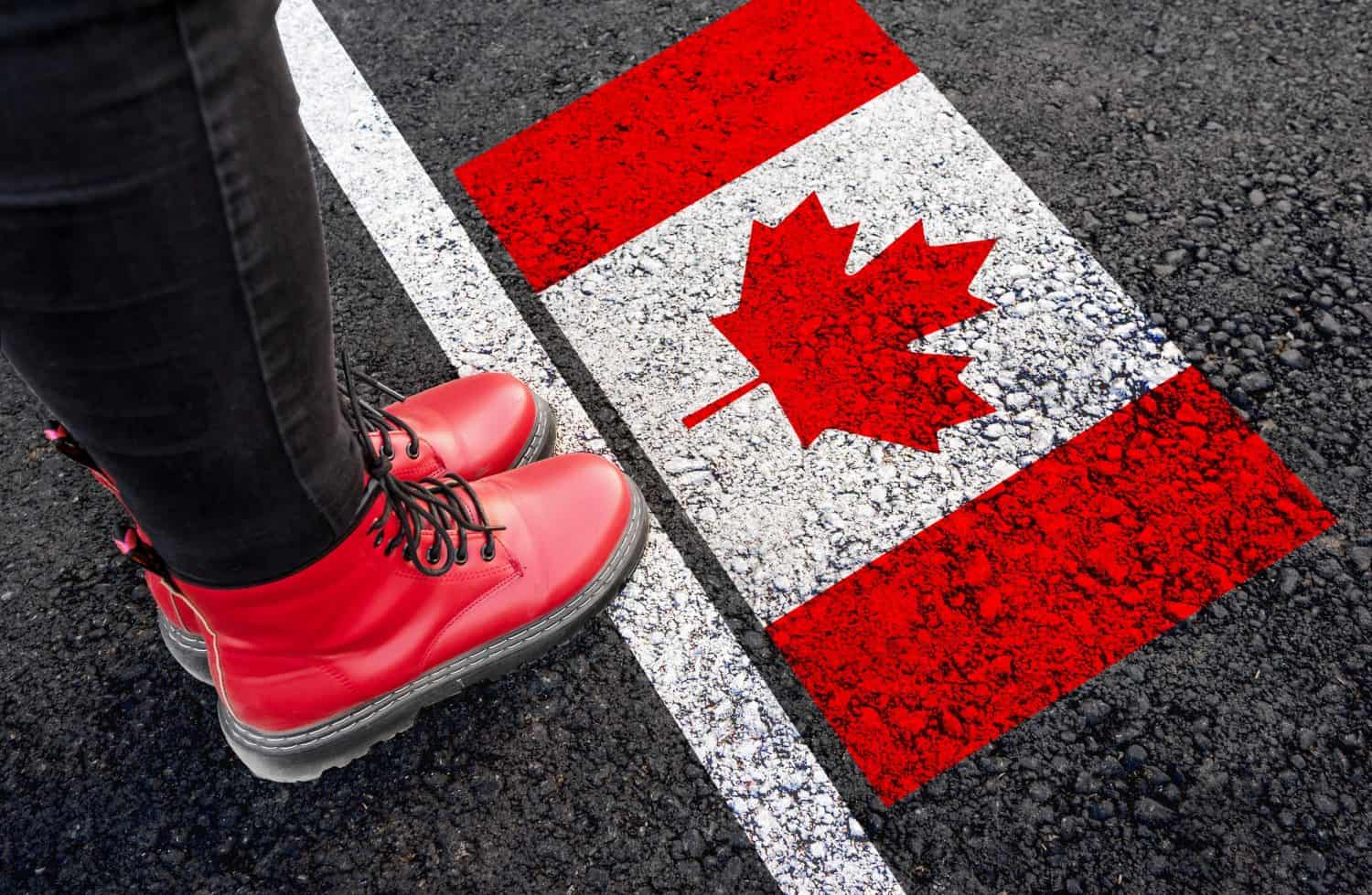 a woman with a boots standing on asphalt next to flag of Canada and border