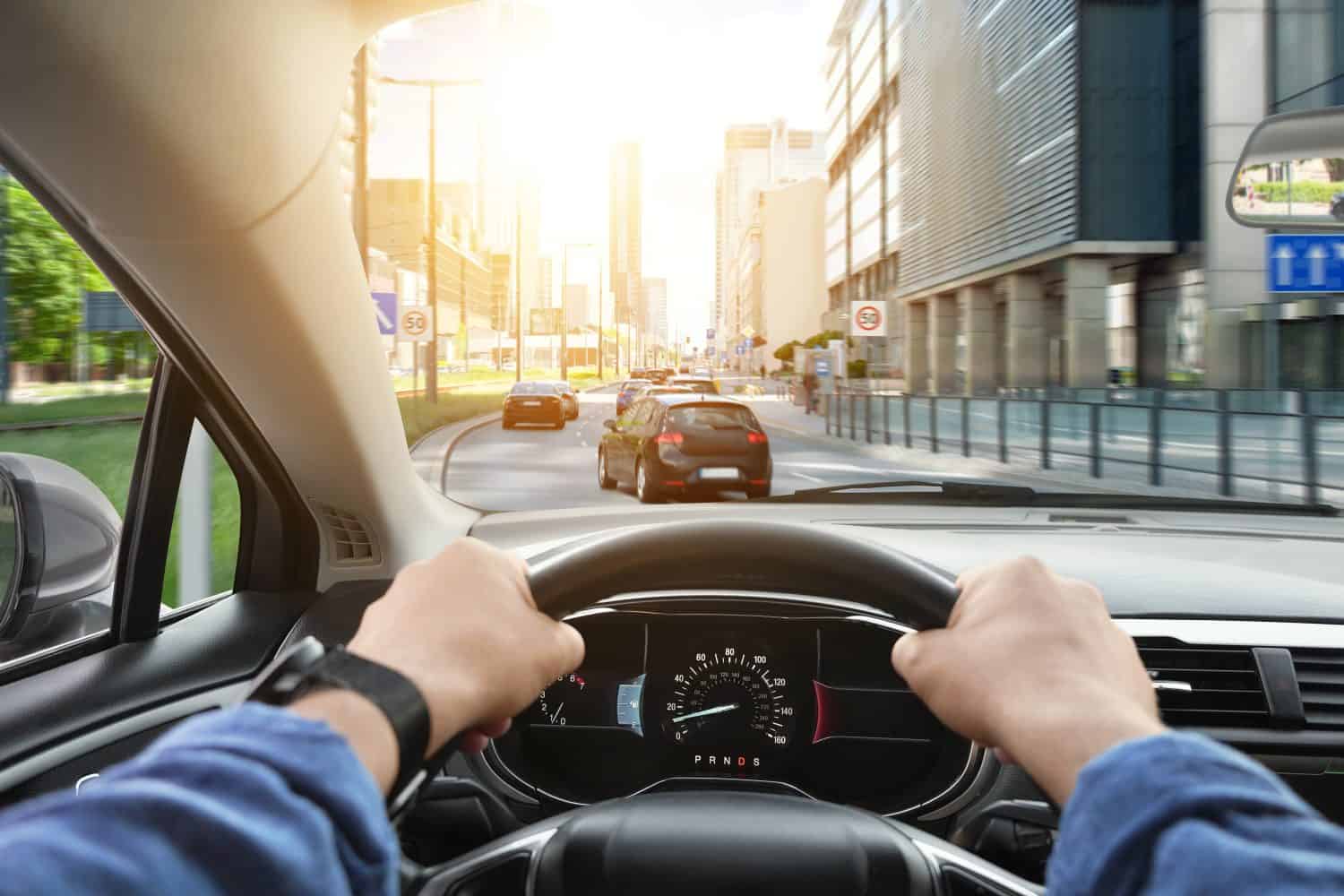 Driving car, view from driver&#039;s seat. Man holding hands on steering wheel, closeup