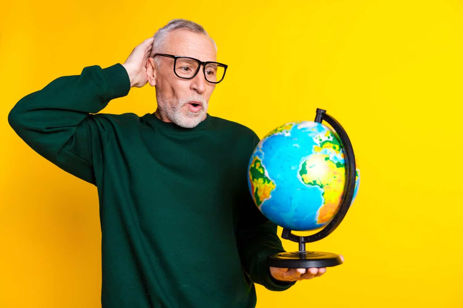 Photo portrait of nice senior man look nervous globe dressed stylish green clothes isolated on yellow color background