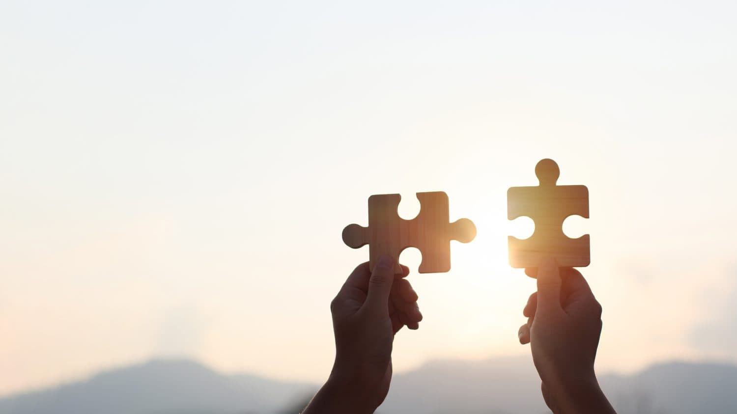 Teamwork and partnership concept. Hands are raised against a bright, white sky, each holding a piece of a wooden jigsaw puzzle. teamwork, problem-solving, Charity, volunteer. Unity, team business.