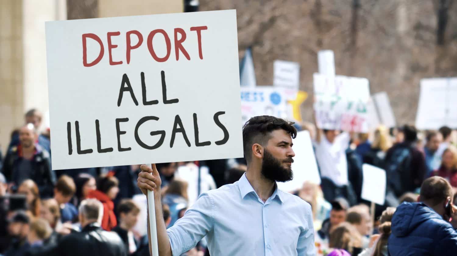 Angry man hold deport all illegals banner. Immigration crisis protest. Crowd wave placard. Stop no immigrants deportation. Anti migration demonstration. Guy against migrants. Refugee march city street