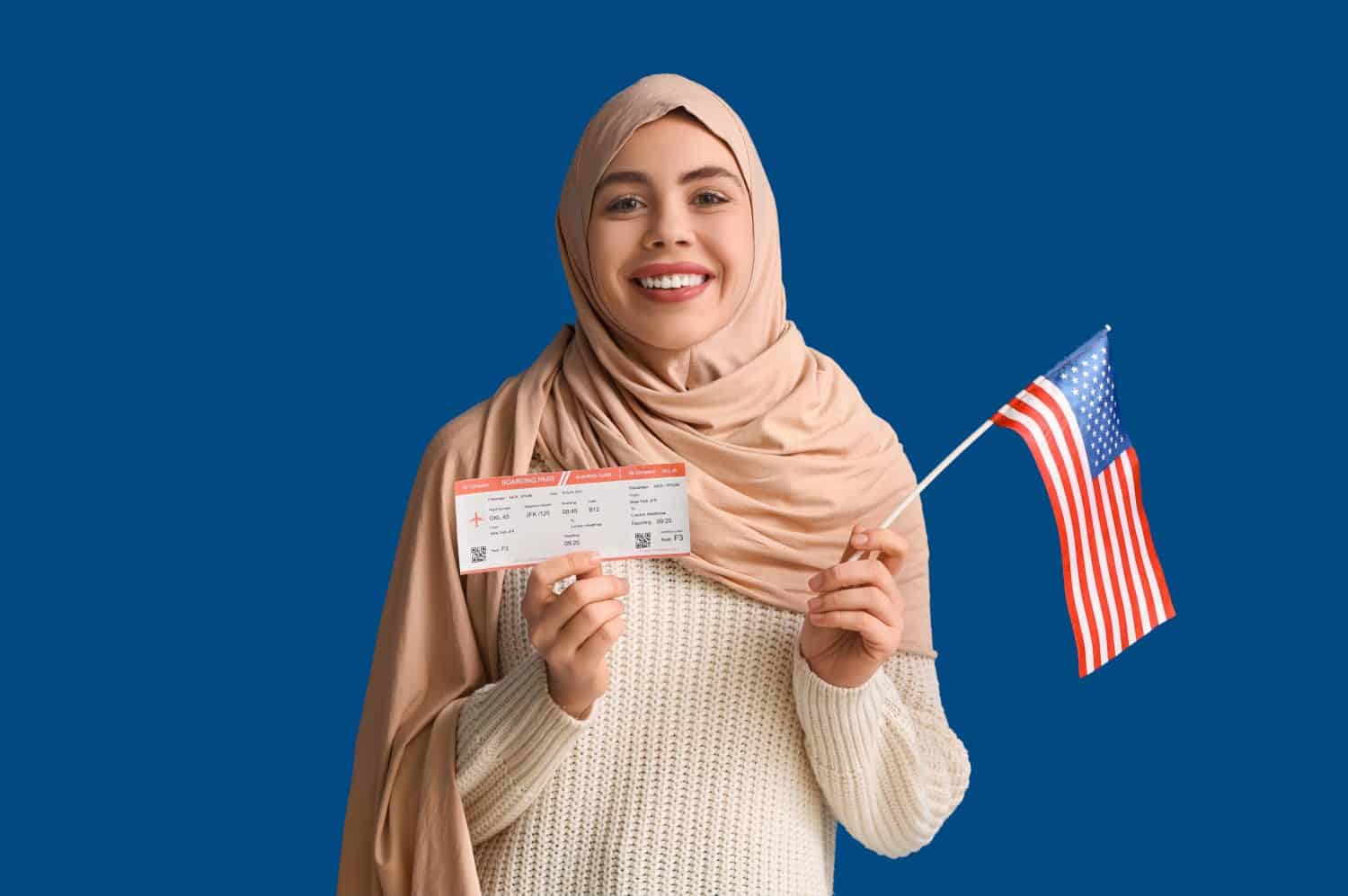 Beautiful young happy Muslim woman with USA flag and ticket on blue background