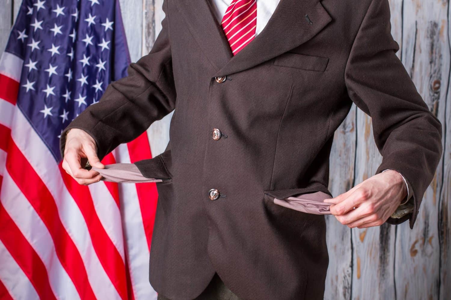 Businessman shows empty pockets. US flag behind man&#039;s back. Crisis came suddenly. Governor has too many debts.