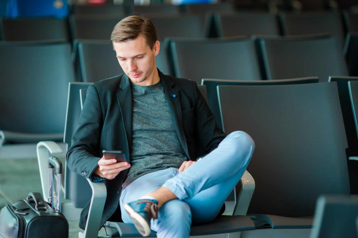 Urban business man talking on smart phone traveling inside in airport. Casual young businessman wearing suit jacket. Handsome male model. Young man with cellphone at the airport while waiting for