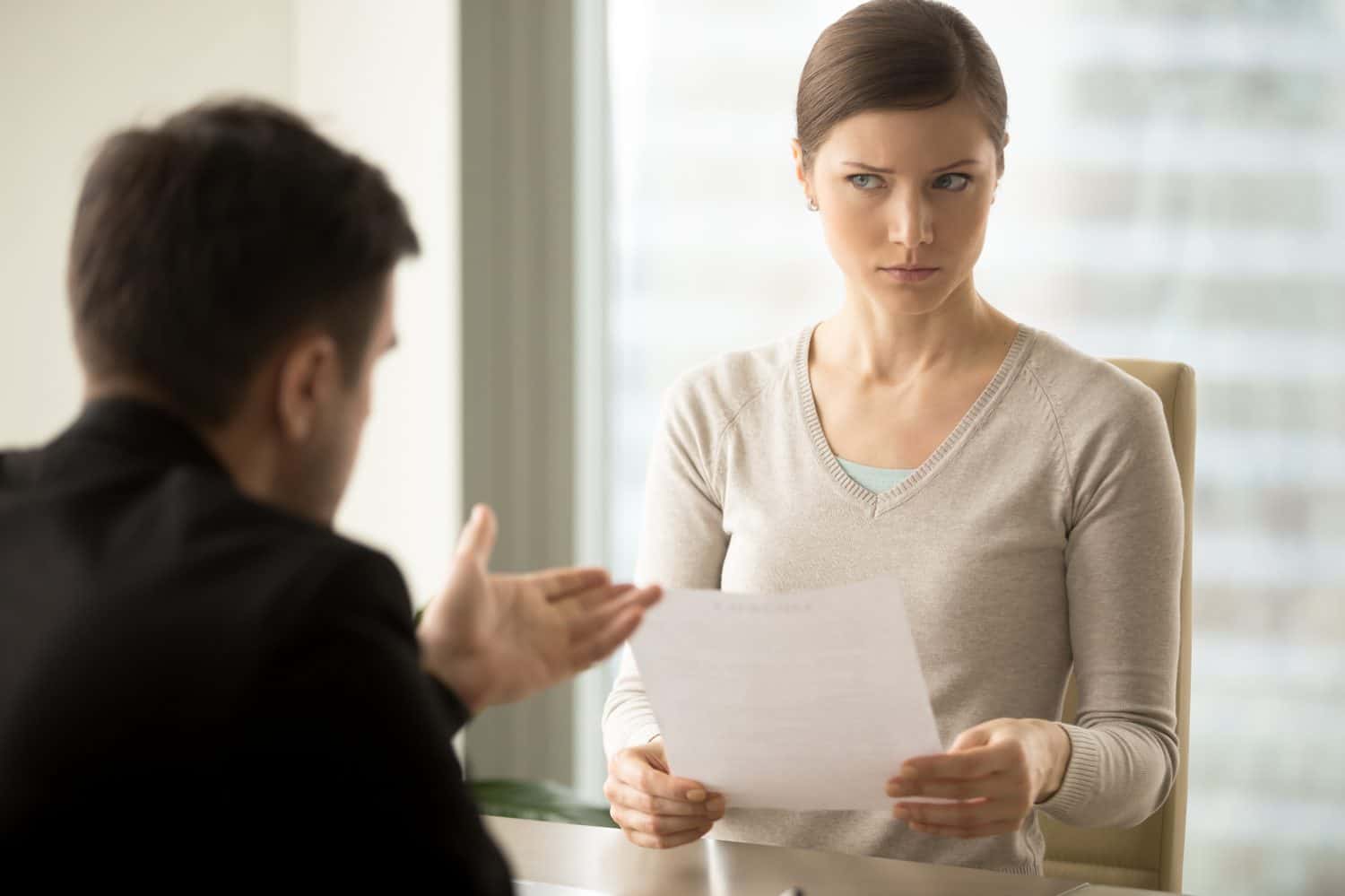 Millennial businesswoman with skeptical facial expression holding contract document and listening unconvincing offer of business partner. Suspicious terms of agreement, doubtful investor, fraud, scam