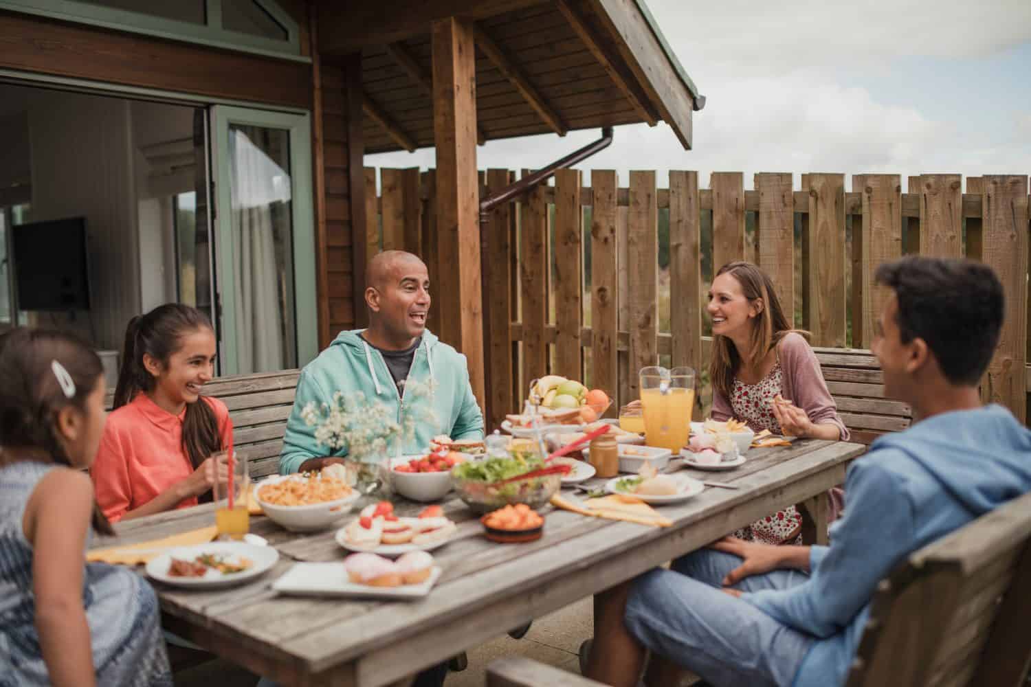 Family bonding and laughing, sitting having breakfast outside holiday cottage.