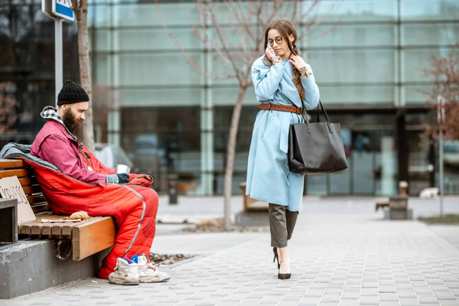 Homeless begging money while sitting on the bench with passing by businesswoman near the business center