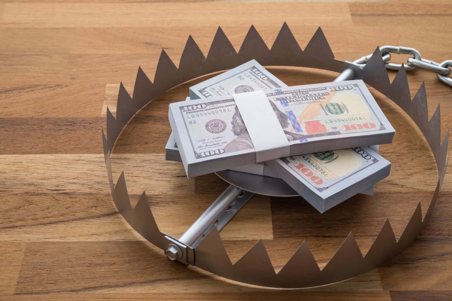 Pile of money dollar banknotes in trap on wooden table background. Concept of financial risk management, loss in stock market, money investment or personal loan.