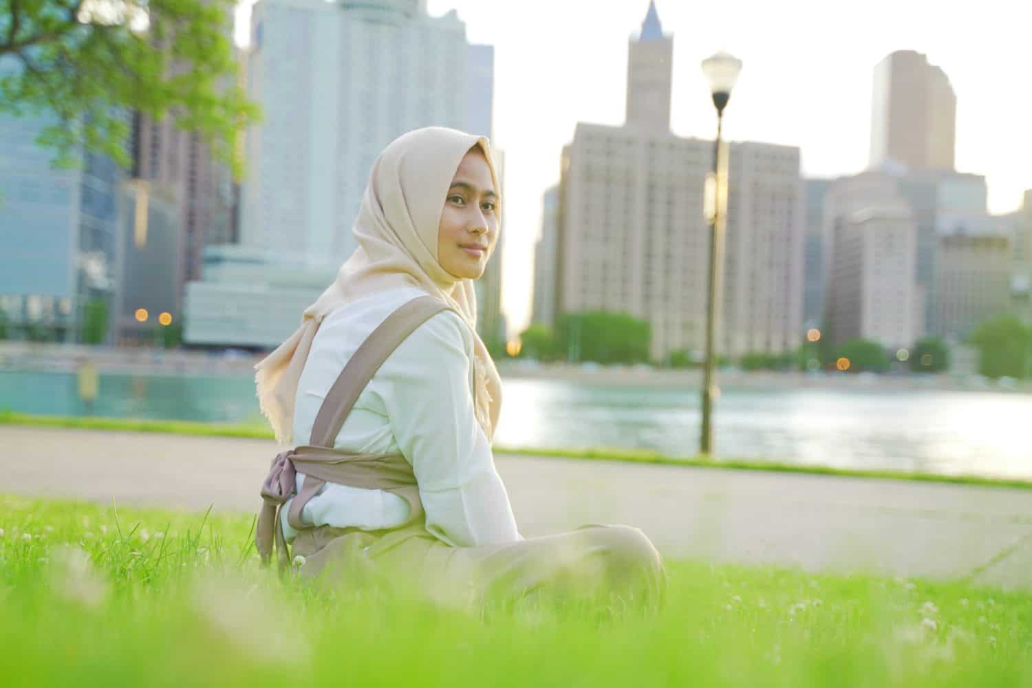 Beautiful and happy young moslem woman sitting at the chicago park in a sunny day with the green grass