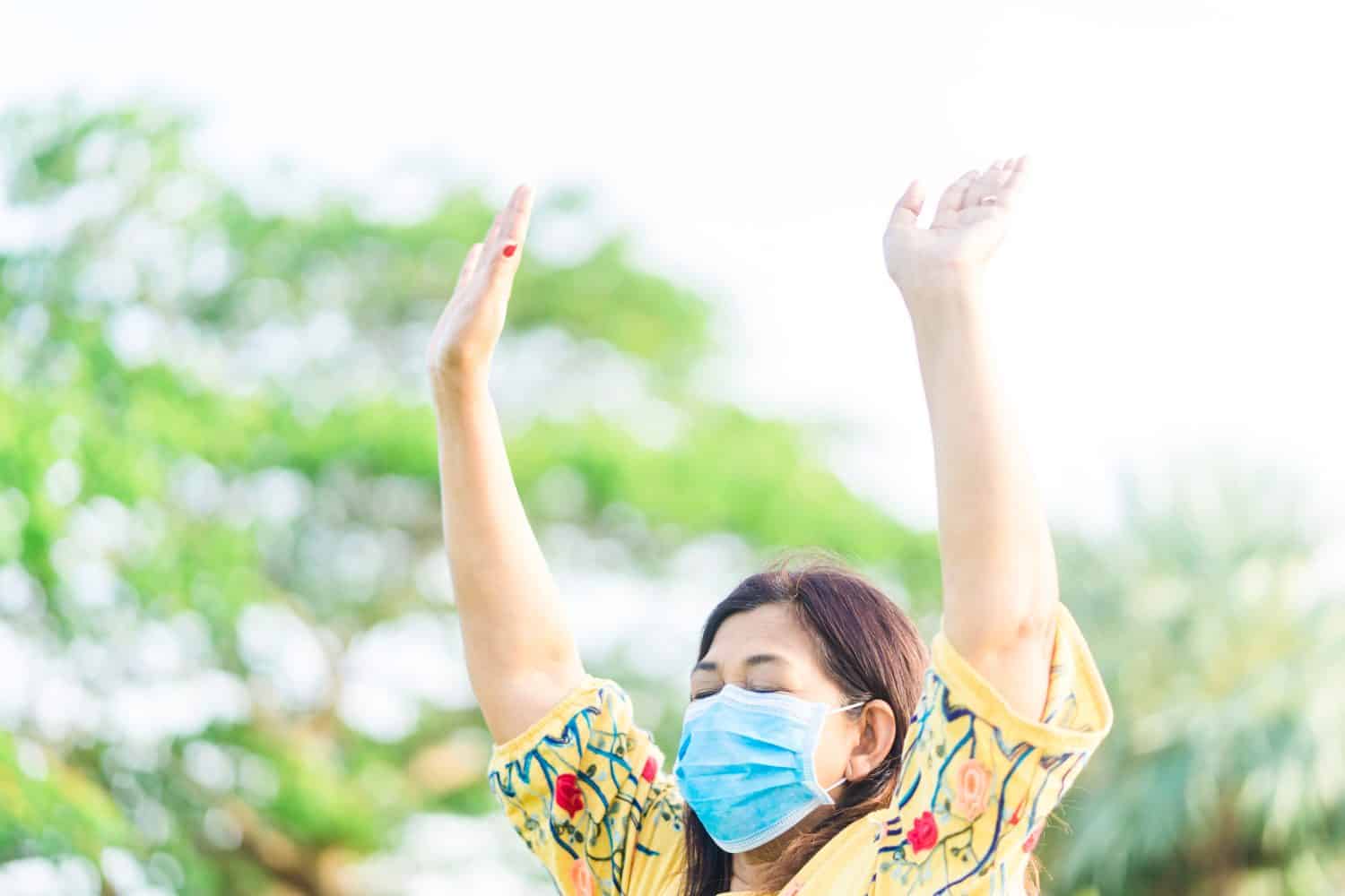 Senior 58 years old indian woman wearing mask for protect coronavirus Covid-19 virus.She praying in the morning for a new day freedom to Covid19 virus.Old woman hand praying for thank GOD.Copy space.