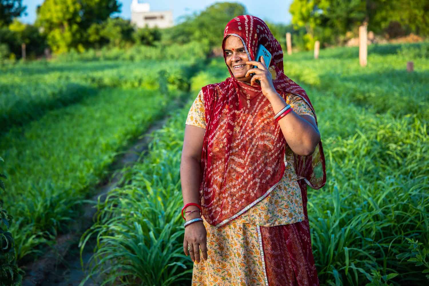 Rural indian woman talking on mobile phone standing at agriculture field, happy Village of india. Use of wireless technology, Telecom industry. Communication device. Cell phone.