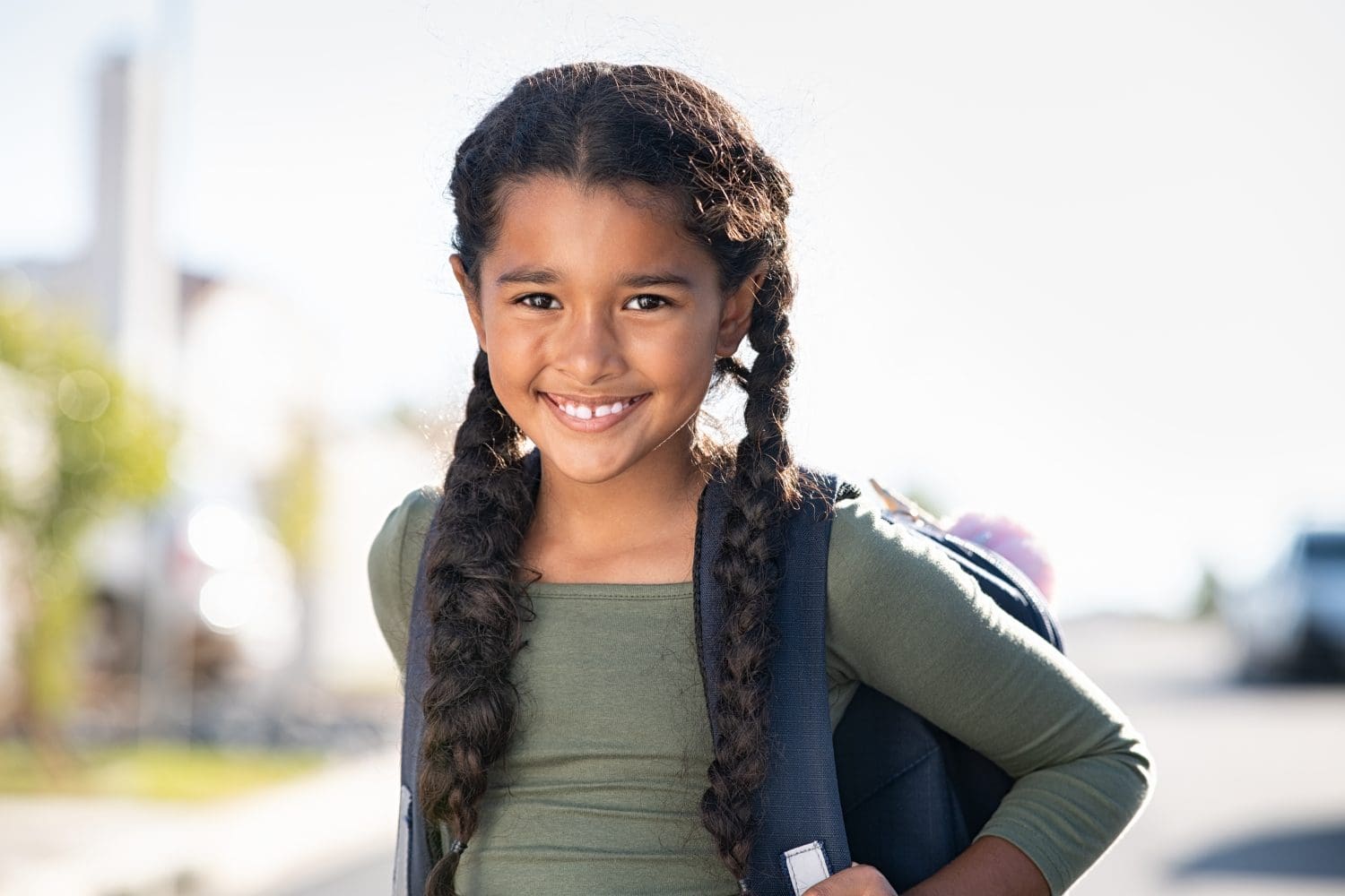 Portrait of happy indian girl with school bag standing outdoor. Little happy schoolgirl going to school, back to school, education concept. Cute mixed race female student smiling and looking at camera