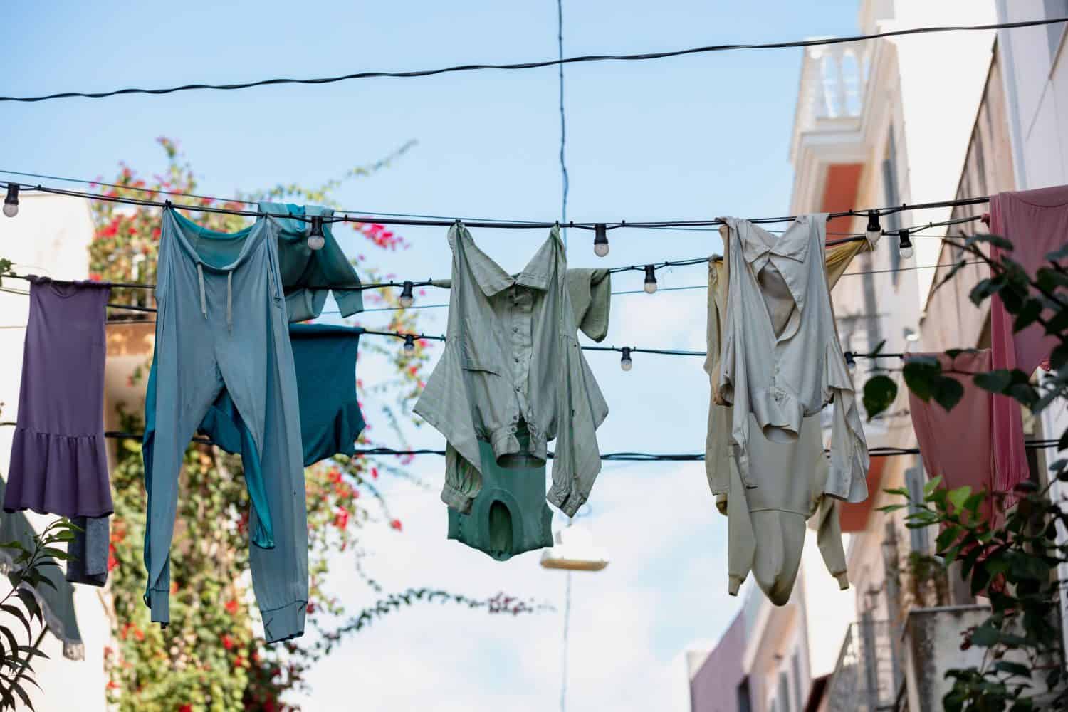 Shabby garments hanging and drying on electric cables with light bulbs against blue sky in Monastiraki street. Athens Greece. Cloths natural old fashioned drying