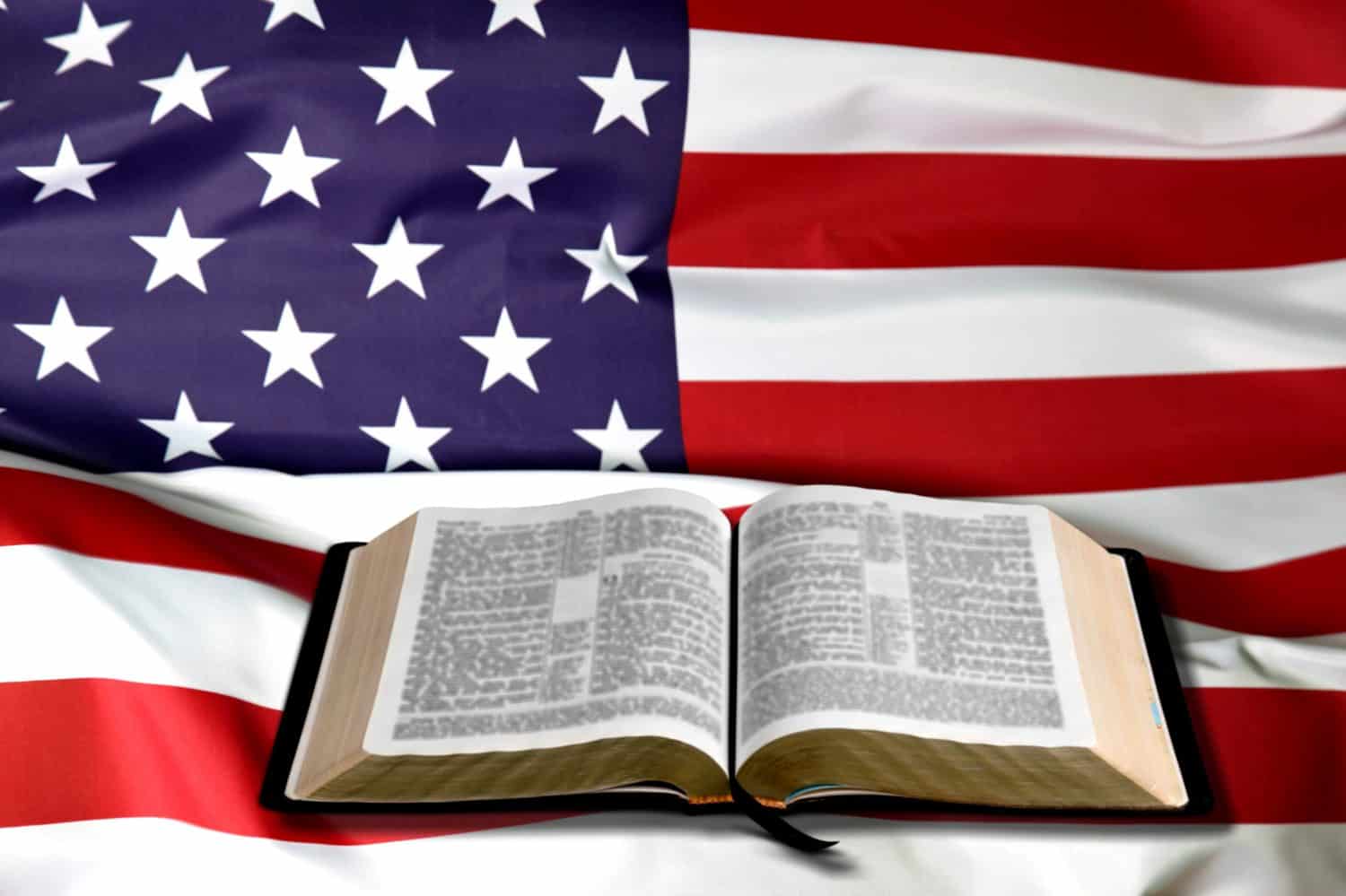 Open is reading Holy Bible book with an American flag on wooden table