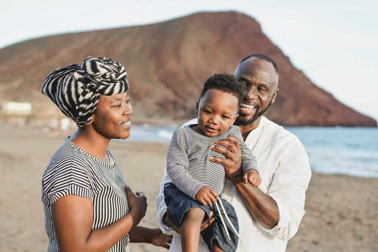 Black family having fun on the beach - African mother, father and toddler love