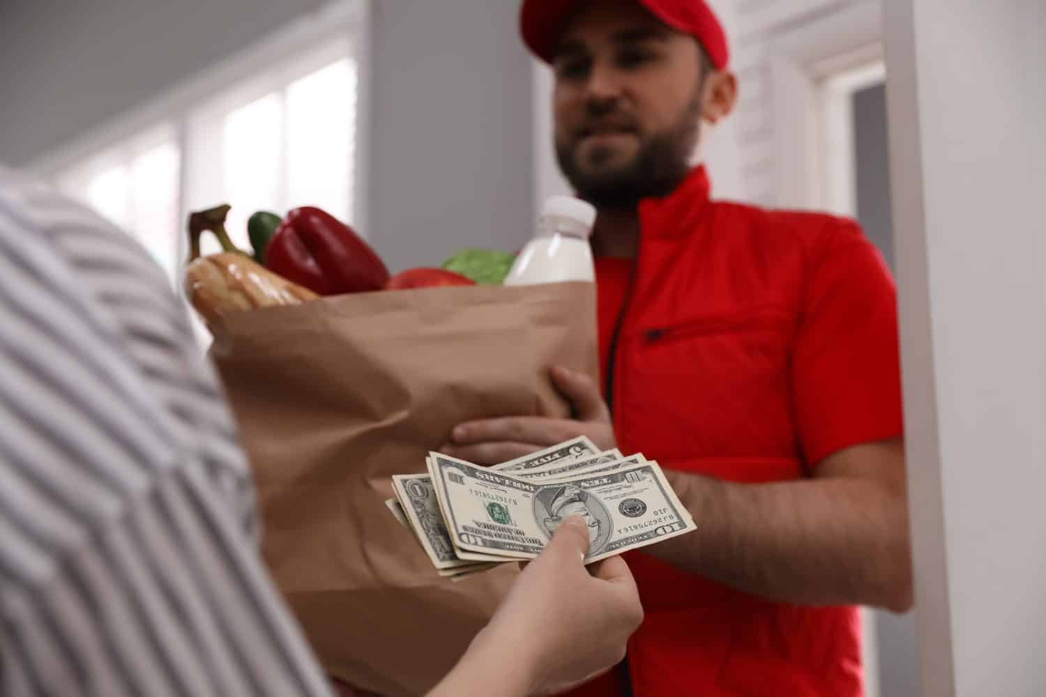 Young woman giving tips to courier indoors, closeup