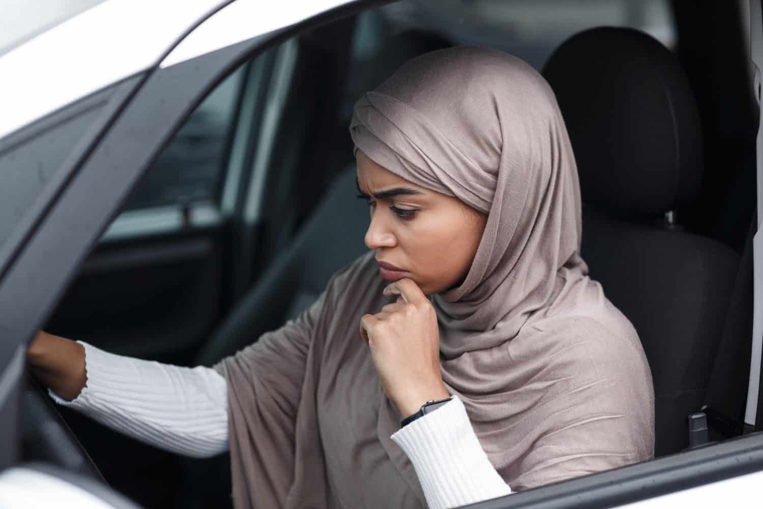 Depressed attractive islamic african american woman driver in hijab driving car, stop and waiting for movement, profile. Sad of traffic jams in city, accident, crash, problem of incident on road