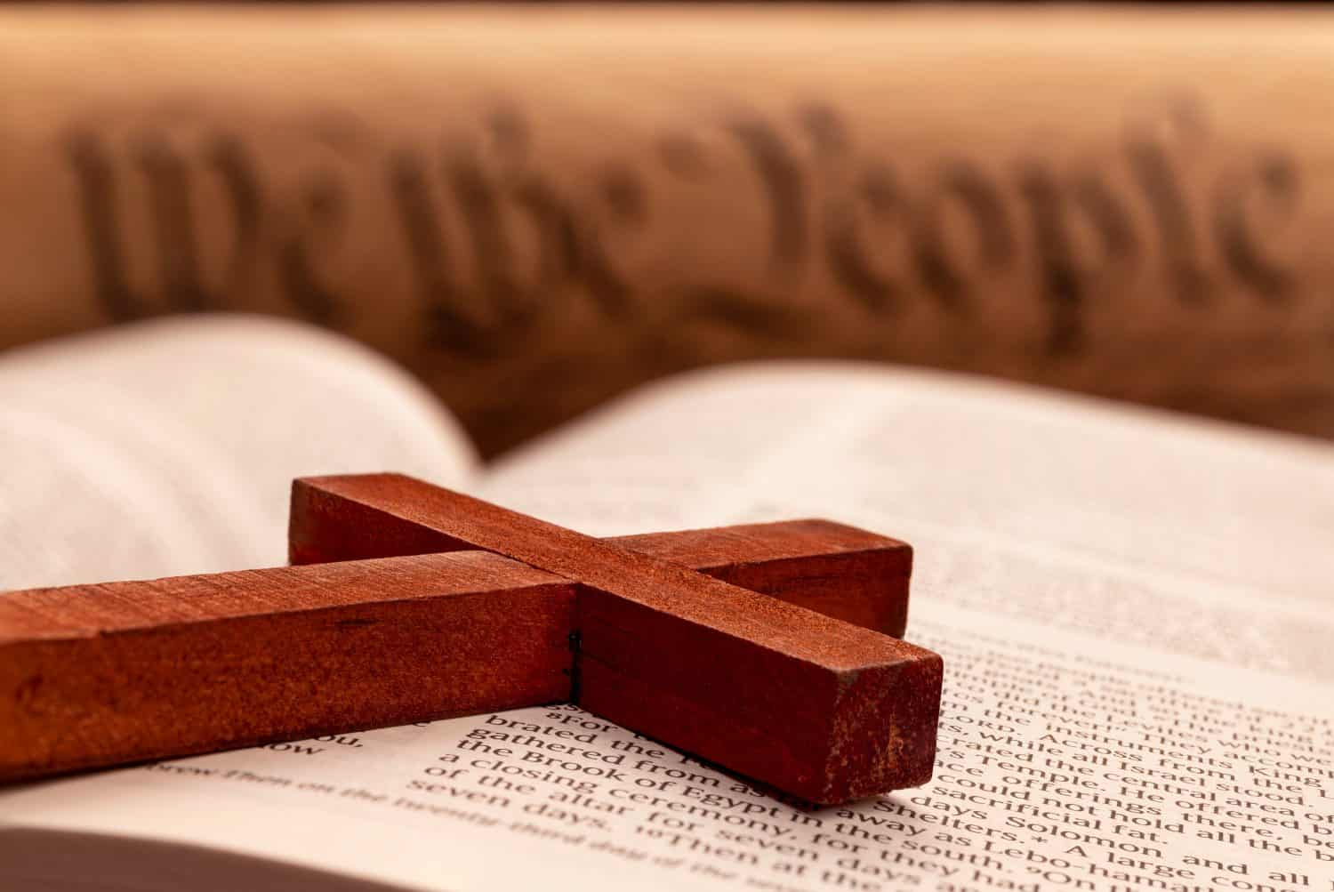 Close up of a religious cross atop the pages of a bible with the constitution in the background.