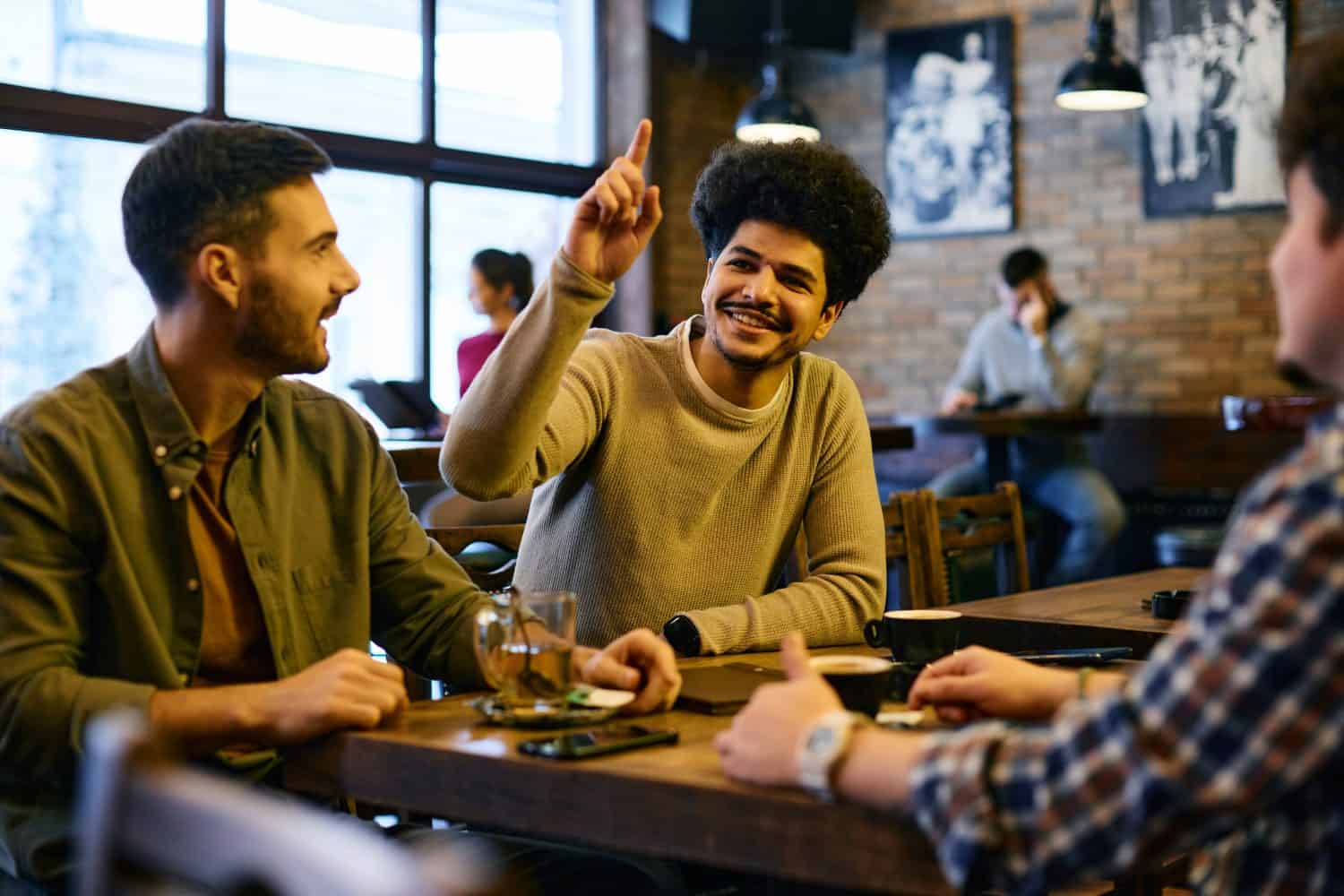 Group of multiracial friends making order in a pub. Focus is on Lebanese man with hand raised calling the waiter.