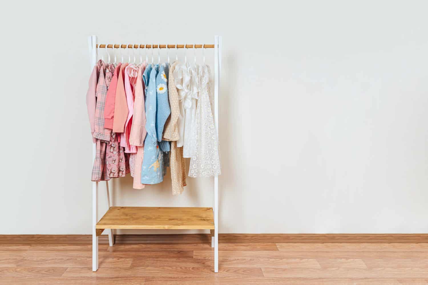 Wooden Clothing Rack with children&#039;s dresses, sweaters and jacket in kids room. Montessori wardrobe. Nursery Storage Ideas. Baby Girl Clothes.