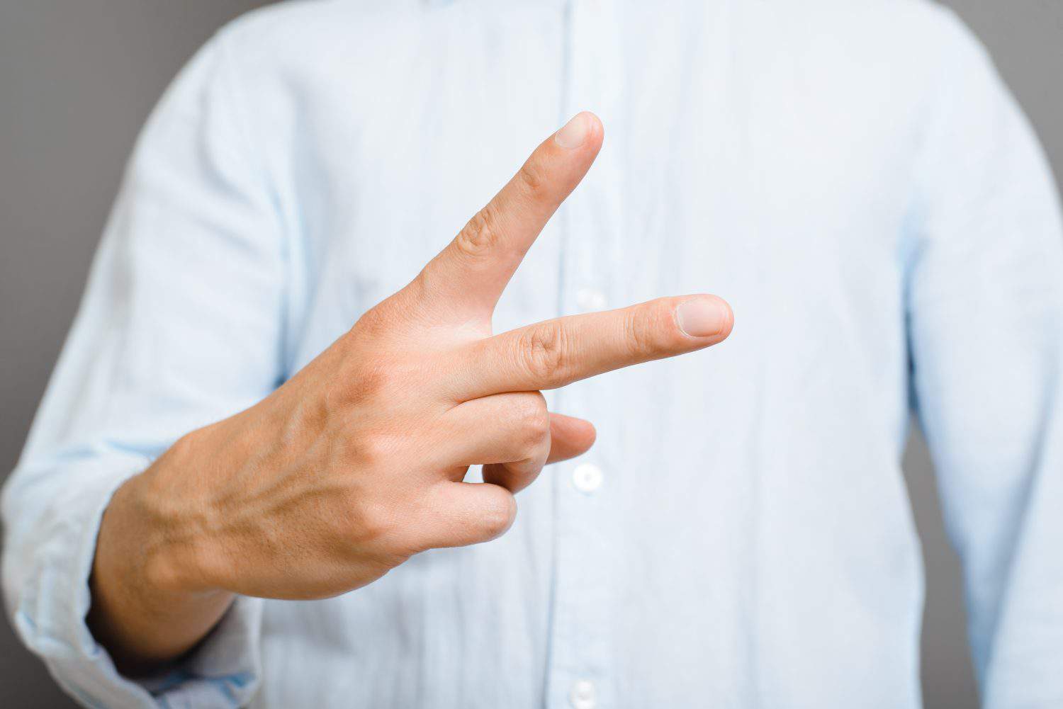 Symbol of peace, sign of victory. Close-up of an unrecognizable man in blue shirt showing two fingers.