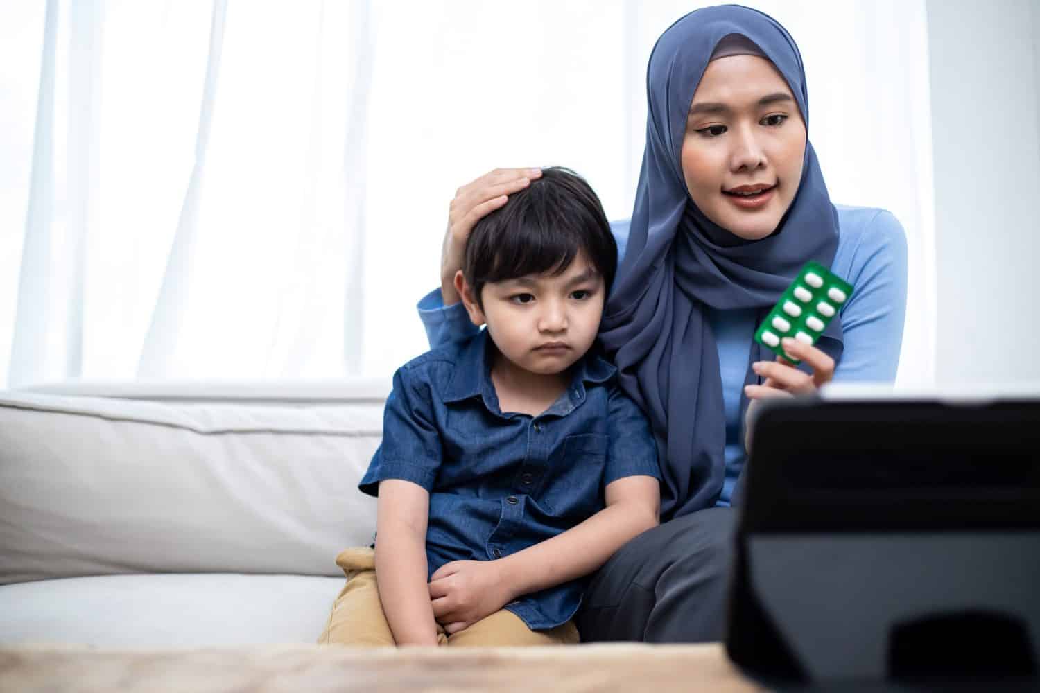 Young Asian muslim parents and son talk to doctor on cellphone videocall conference medical app in pediatric care online telehealth telemedicine. Home health care.