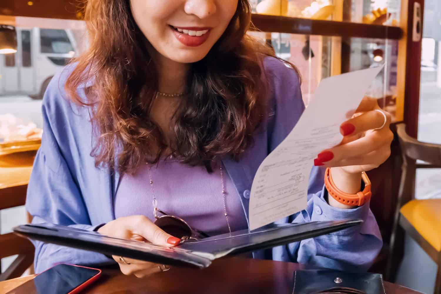 Happy customer girl looking at bill receipt after dinner in luxury restaurant