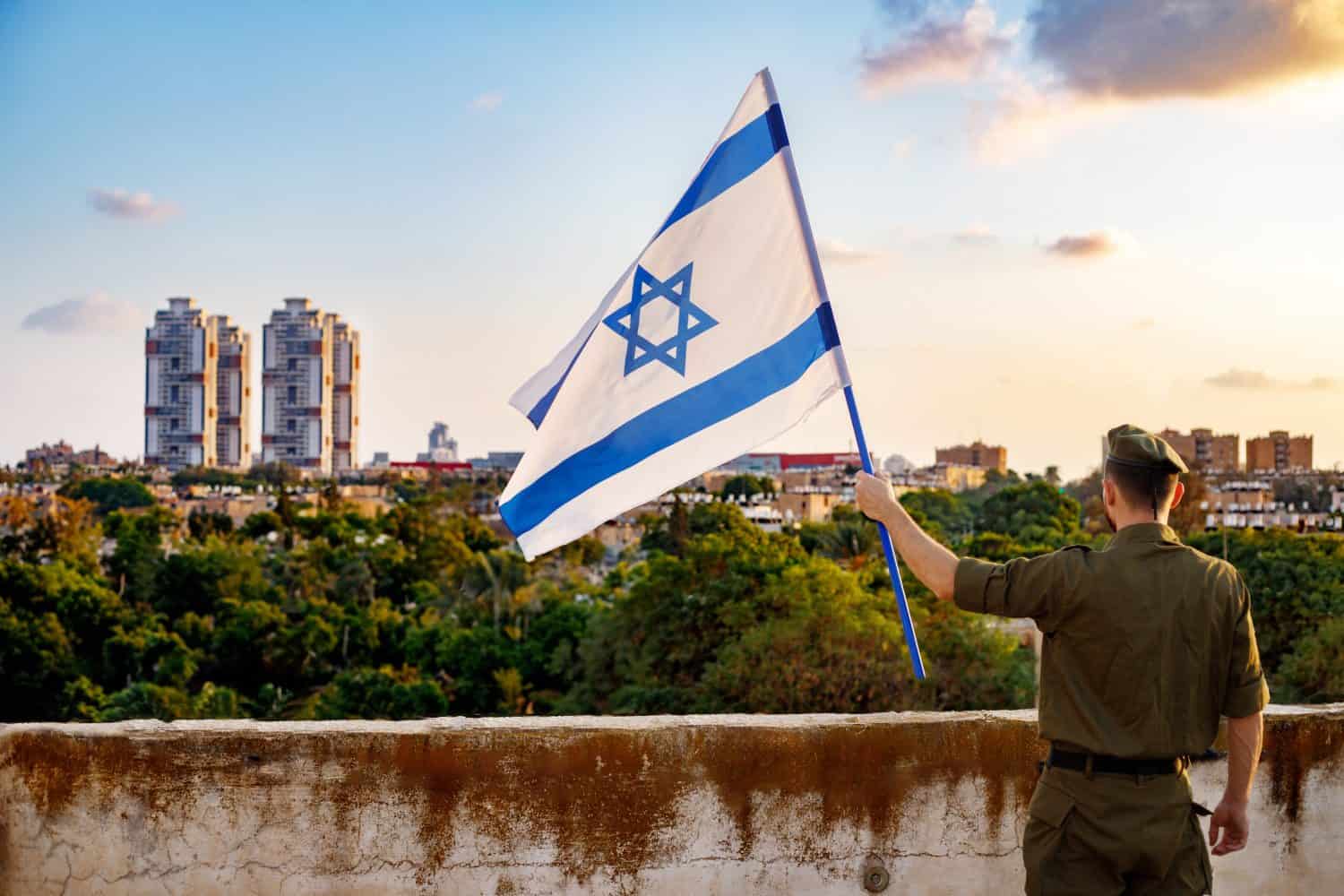 A guy in a soldier&#039;s uniform with an Israeli flag in his hand against a cloudy sky. Remembrance Day - Yom HaZikaron, Patriotic holiday, Israeli Independence Day - Yom Ha&#039;atzmaut concept.