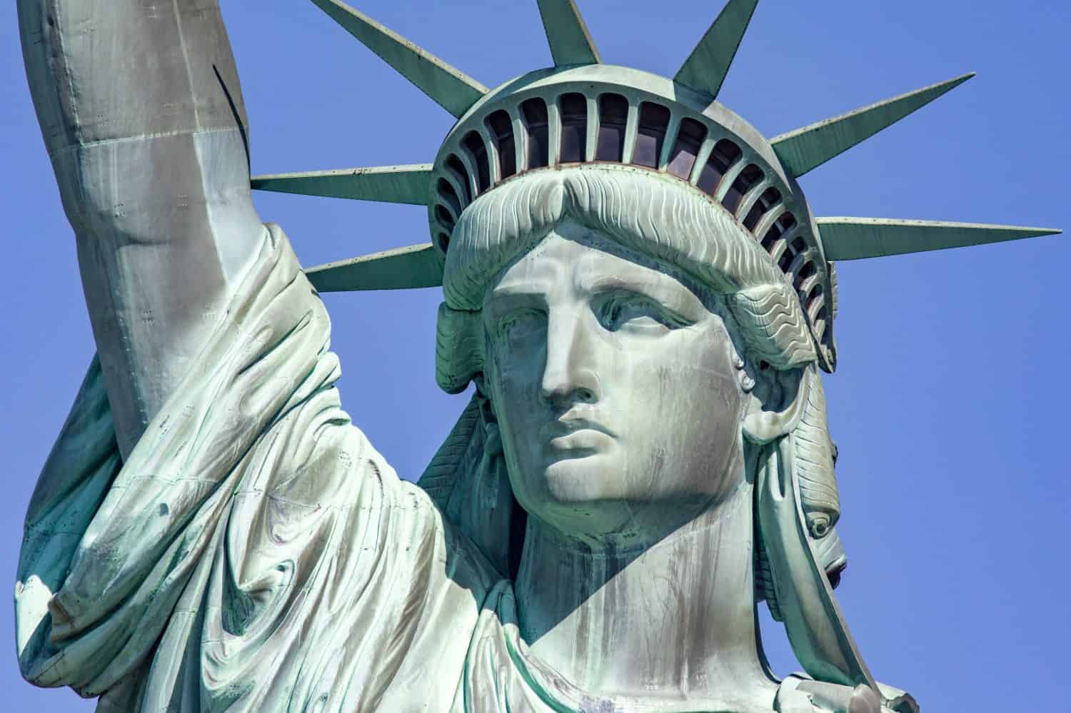 Photograph of the Statue of Liberty holding her torch on a sunny day in Manhattan, known as the lady of New York City and the Big Apple of the USA.