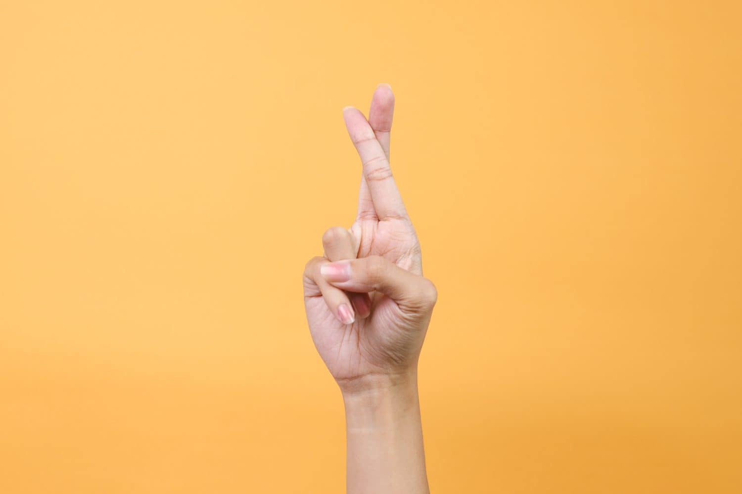 Hand with crossed fingers for luck, isolated on yellow background.