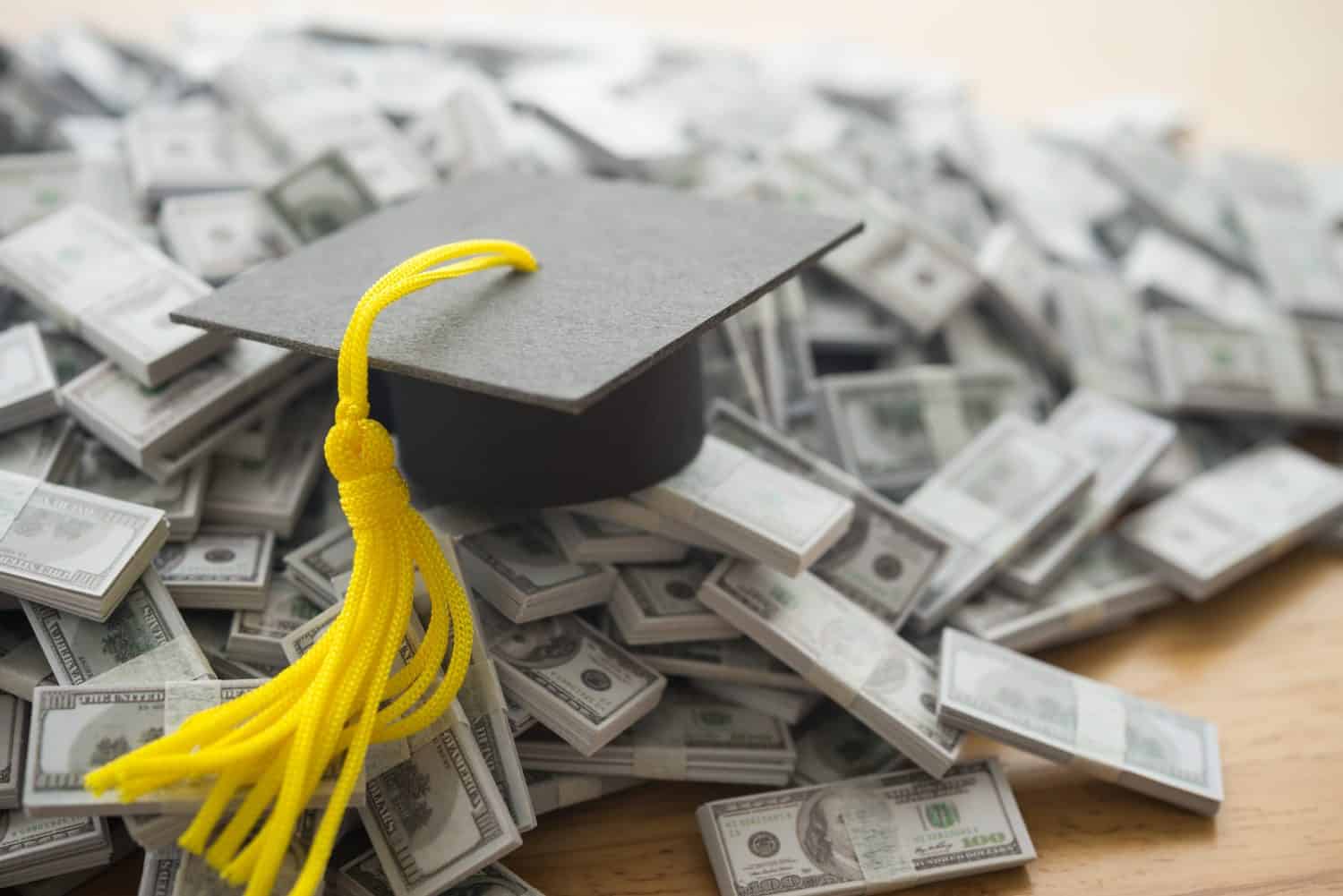 Graduation cap university or college degree on US dollars banknotes pile. Education expense budget plan of money saving, student loan or debt, personal loan, scholarship for studying abroad concept.