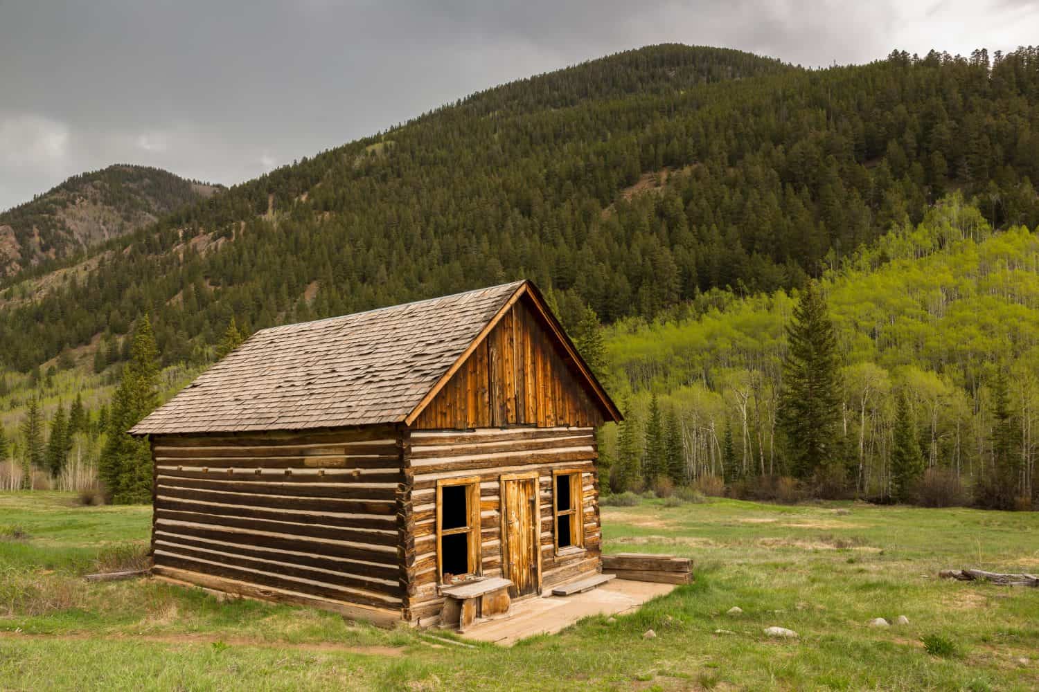A rustic log cabin with mountains in the background.