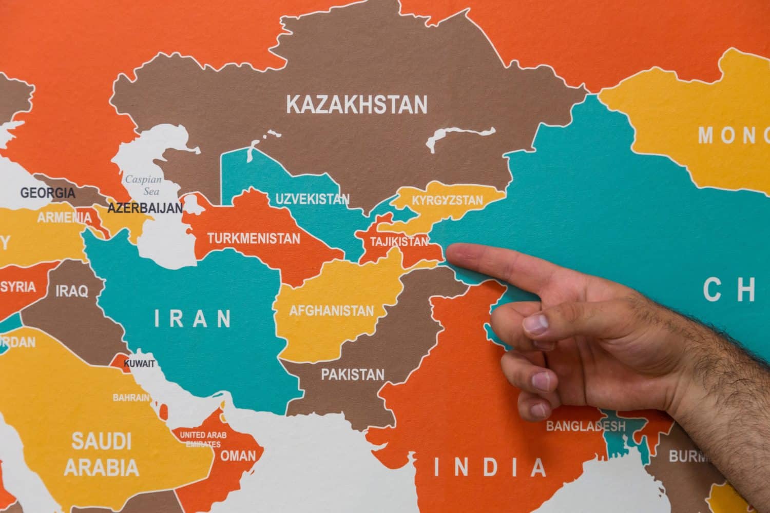 A hand pointing to Tajikistan on a wall map indicating the geographical location and the concept of popular tourist destination and travel.