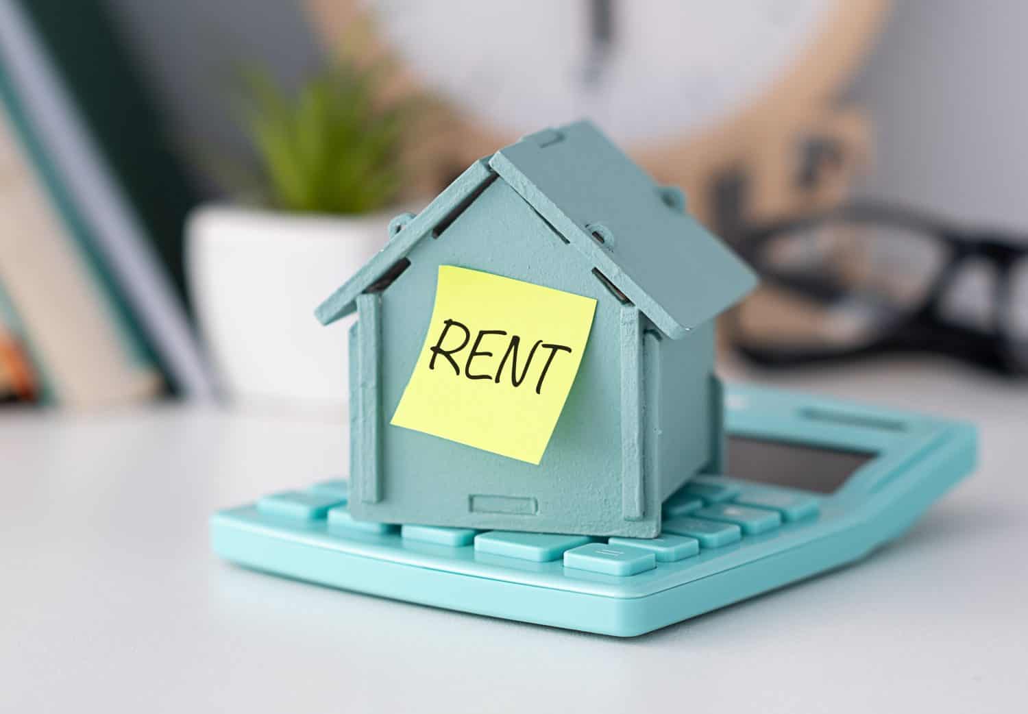 Model house placed on calculator and sticker text Rent. The house has a red roof, It visually represents the concept of renting property