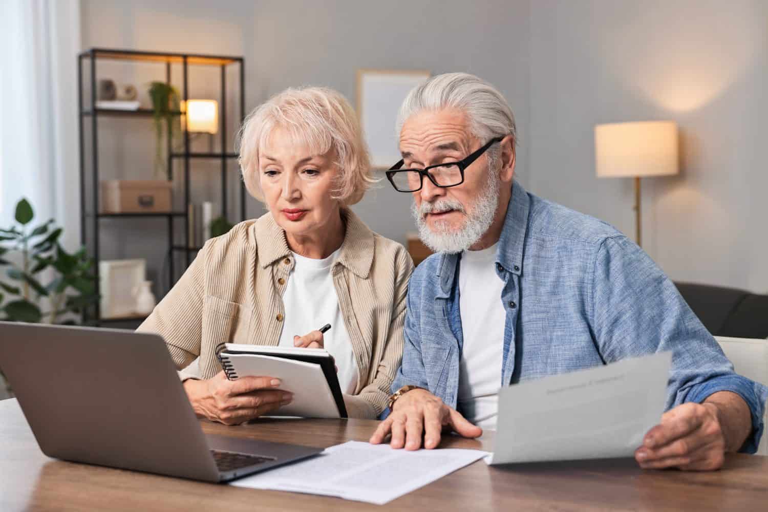 Pension savings. Senior couple planning budget at wooden table indoors